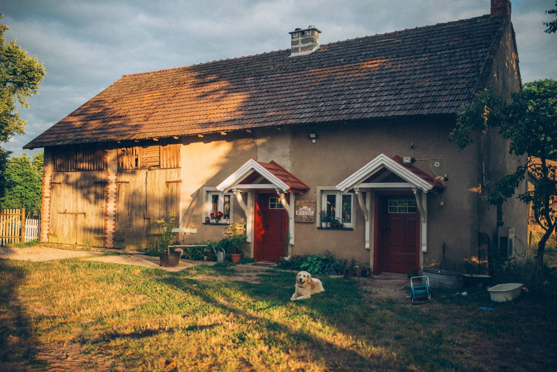 Dom na Kierociu w popołudniowym słońcu, przed nim na trawie leży pies