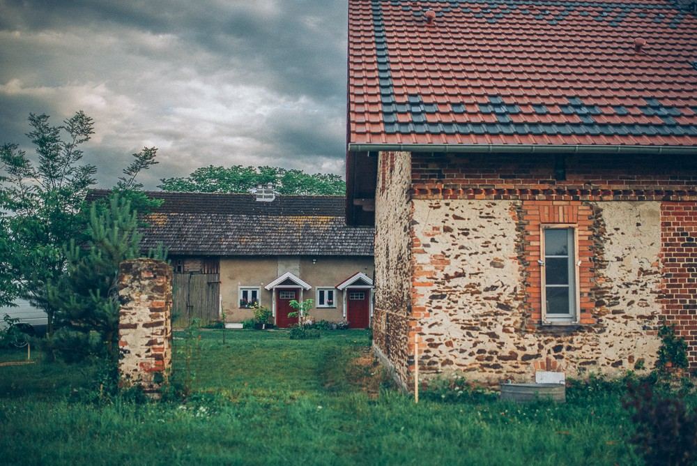 Podwórze na Kierociu: stary dom z czerwonymi drzwiami i kamienno-ceglany budynek gospodarczy